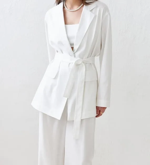 A person in a chic, minimalist outfit (e.g., a cream linen suit) carrying a sleek, structured SHEIN bag in a soft taupe, against a modern architectural background, illustrating polished professional styling.
