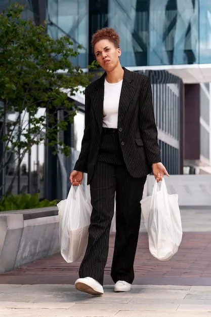 A professional woman in a business-casual blazer and tailored trousers walking purposefully, carrying a structured black SHEIN tote bag with gold hardware, looking confident and business-ready.