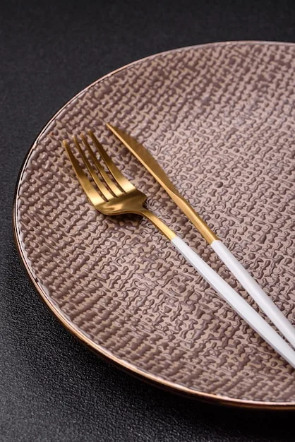 A close-up shot of an elegant SHEIN ceramic plate with a gold rim, paired with simple, modern cutlery, on a textured linen placemat, suggesting a sophisticated US dinner party setting.