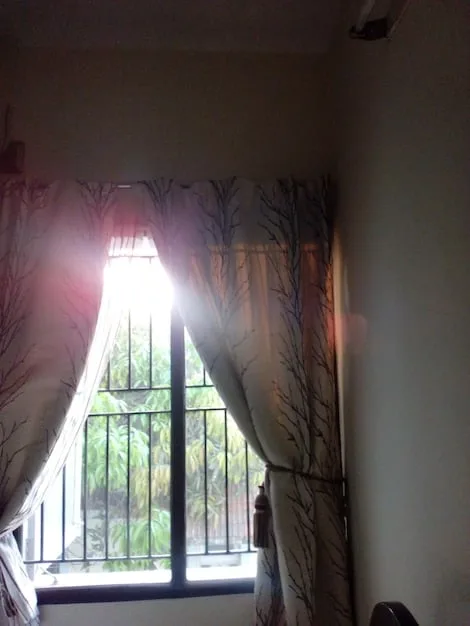 A bedroom window on a sunny morning, showcasing light-blocking SHEIN curtains partially drawn open, allowing soft sunlight to stream in. A cozy bed with crisp linens is visible, emphasizing the curtain's role in creating a serene and private atmosphere.