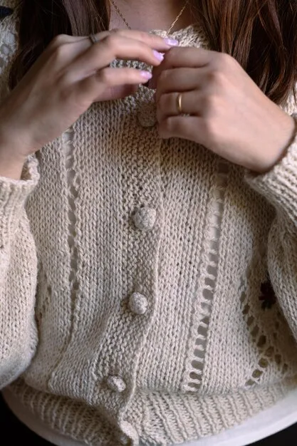 A close-up of hands adorned with delicate layered necklaces and stacking rings, subtly complementing a cozy, neutral-toned cashmere sweater, showcasing modest yet impactful accessory layering.