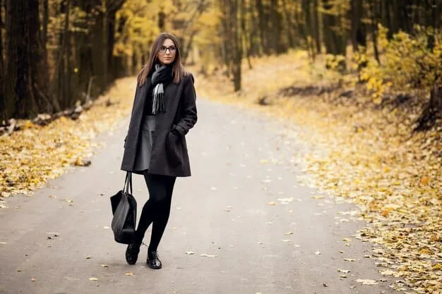 A person wearing classic dark wash straight-leg jeans with a tailored blazer and ankle boots, walking through a city park in autumn.