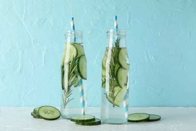 A clear glass water bottle filled with water, sliced cucumbers, and mint leaves. Sunlight streams through, highlighting the freshness.