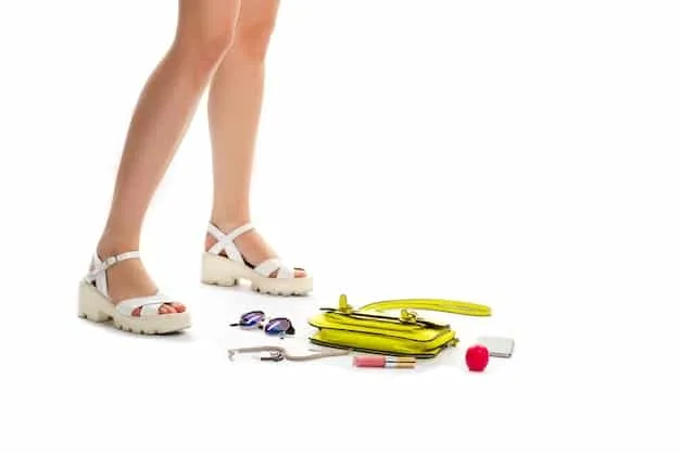 A woman measuring her foot with a tape measure, standing on a white surface, with a pair of sleek heels and a casual sneaker in the background, illustrating the personal process of fitting shoes.