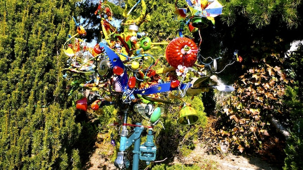 A close-up of an art installation made from recycled materials in a community garden. The artwork is a whimsical sculpture of a bird, constructed from plastic bottles, metal scraps, and colorful fabric pieces. The sculpture is placed amidst lush greenery.