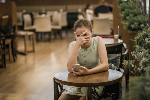 A young student looking distressed while seated alone in a school cafeteria. Other students are nearby, some whispering and pointing in the student's direction. The image evokes a sense of isolation and potential bullying, highlighting the need for intervention and support.