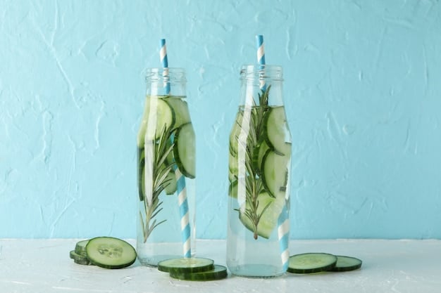 A clear glass water bottle filled with water, sliced cucumbers, and mint leaves. Sunlight streams through, highlighting the freshness.