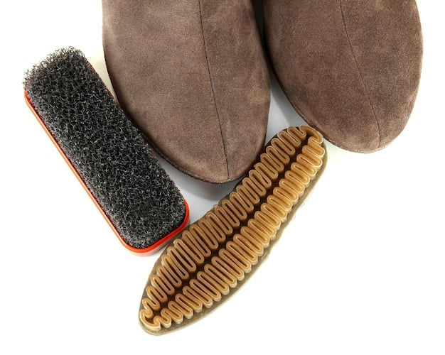 A perfectly arranged collection of shoe care cleaning tools: a soft-bristle brush, a clean white microfiber cloth, a small bottle of shoe cleaning solution, and a spray bottle, all against a neutral background.
