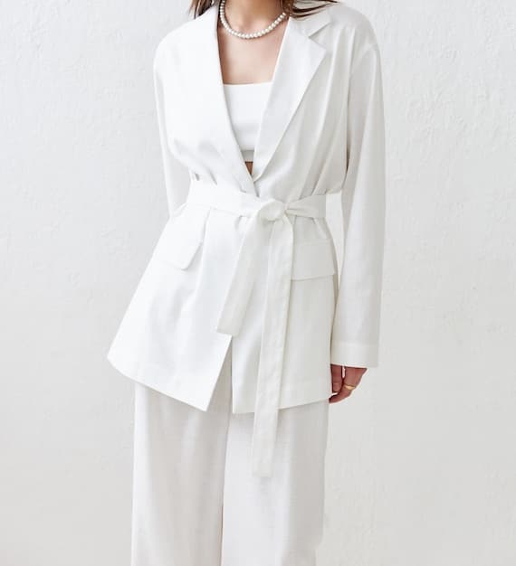A person in a chic, minimalist outfit (e.g., a cream linen suit) carrying a sleek, structured SHEIN bag in a soft taupe, against a modern architectural background, illustrating polished professional styling.