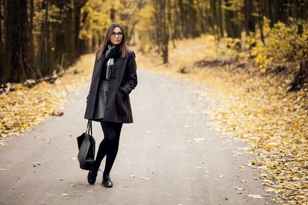 A person wearing classic dark wash straight-leg jeans with a tailored blazer and ankle boots, walking through a city park in autumn.