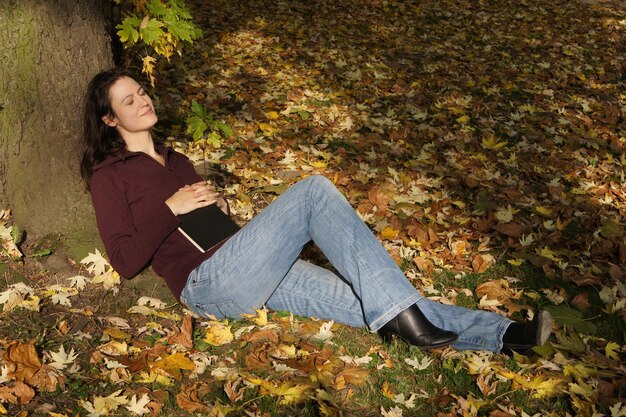 A person wearing high-waisted flared jeans in a medium wash, paired with a fitted knit top and block-heel boots, against a backdrop of autumn leaves.