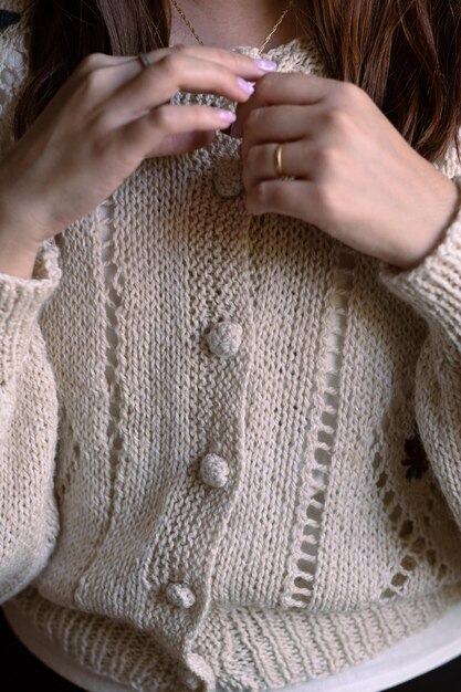 A close-up of hands adorned with delicate layered necklaces and stacking rings, subtly complementing a cozy, neutral-toned cashmere sweater, showcasing modest yet impactful accessory layering.