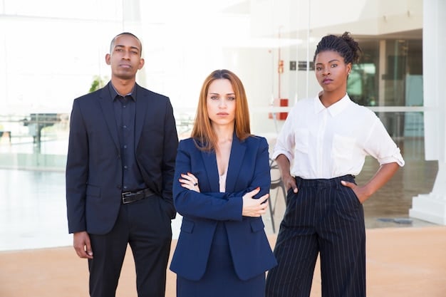A diverse group of men and women in smart business attire, standing confidently in a modern office space, showcasing professional collaboration.